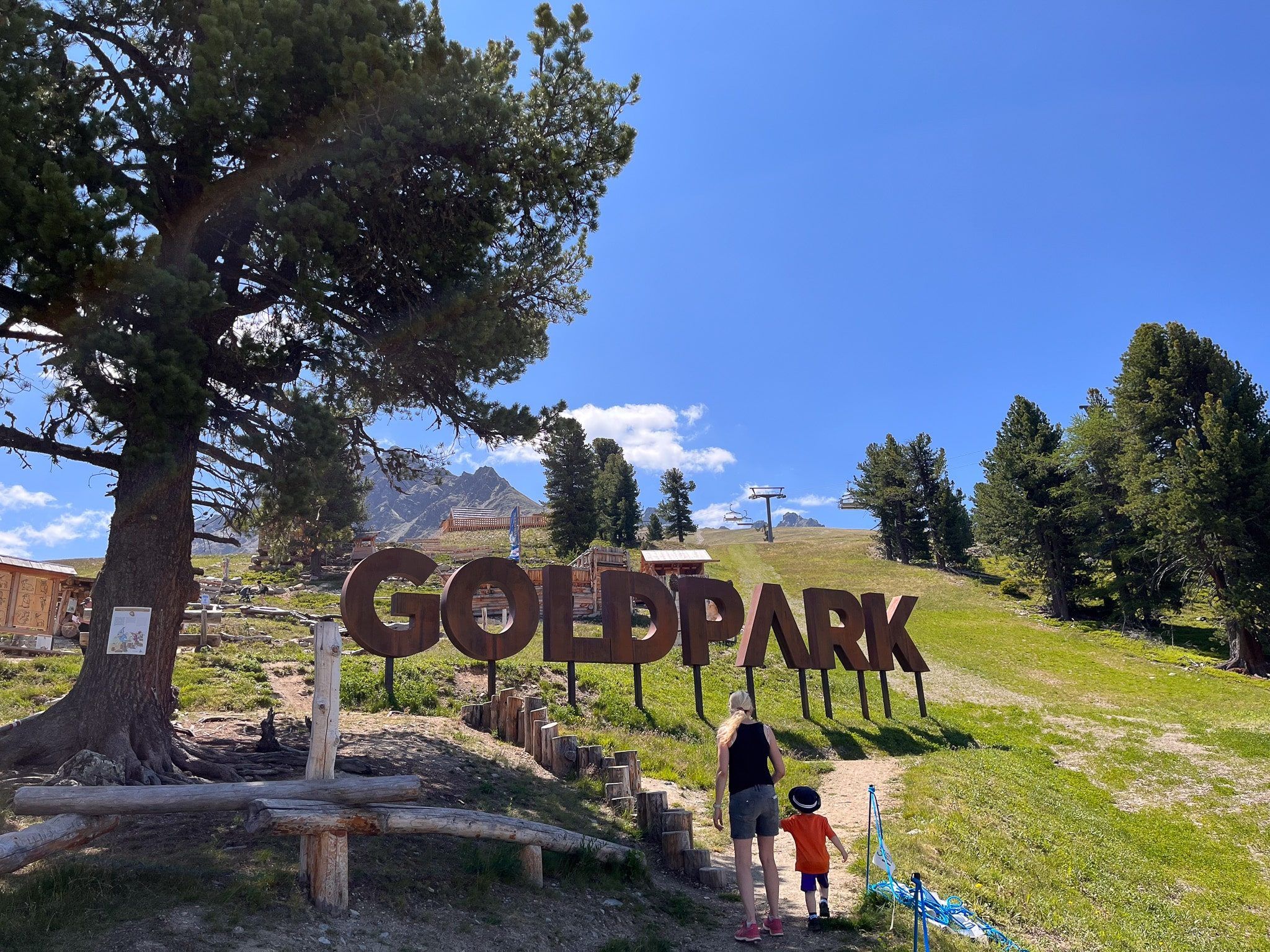 Mutter und Kind vor dem Holzschriftzug Goldpark auf der Alm in Nauders