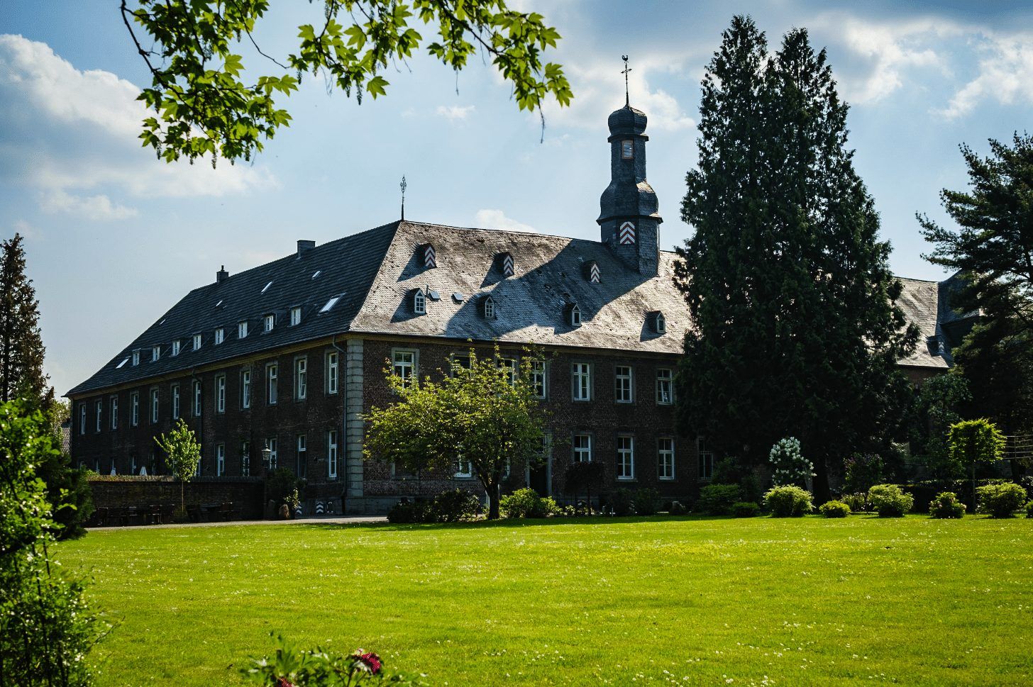 Das Nikolauskloster in Jüchen mit Rasen und Bäumen unter blauem Himmel