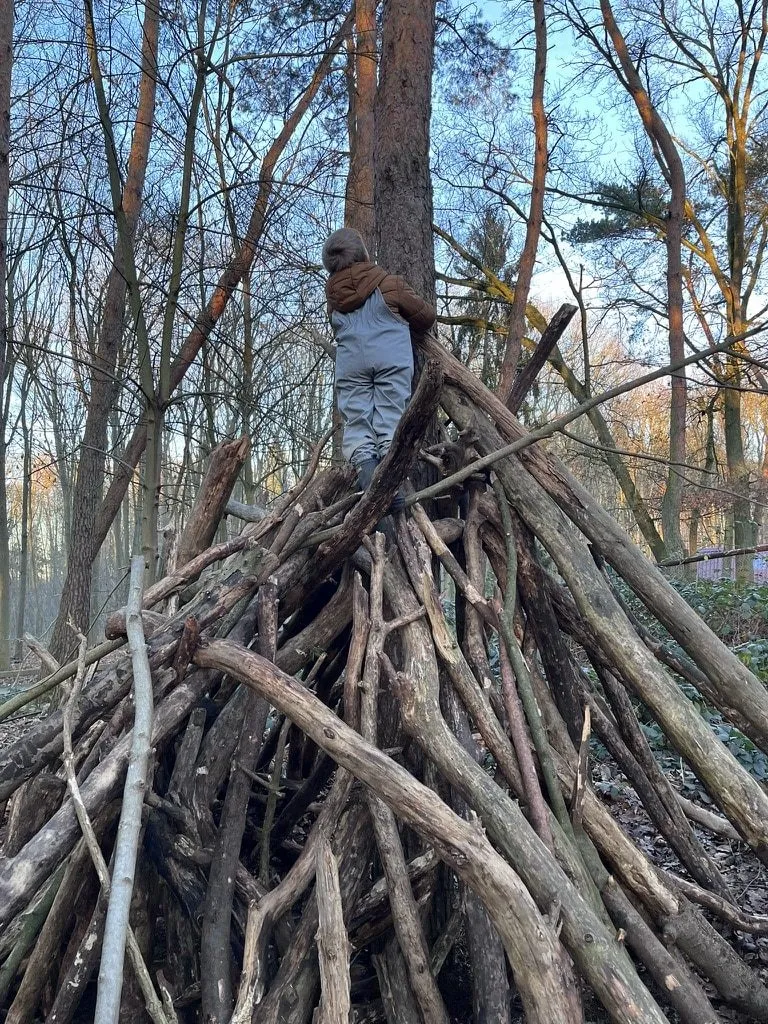 Kind klettert auf ein Tipi aus Baumstämmen