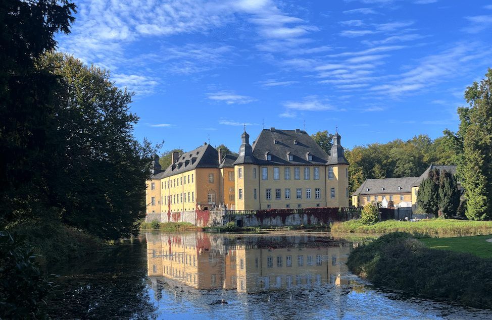 Schloss Dyck spiegelt sich im Schlossweiher unter blauem Himmel